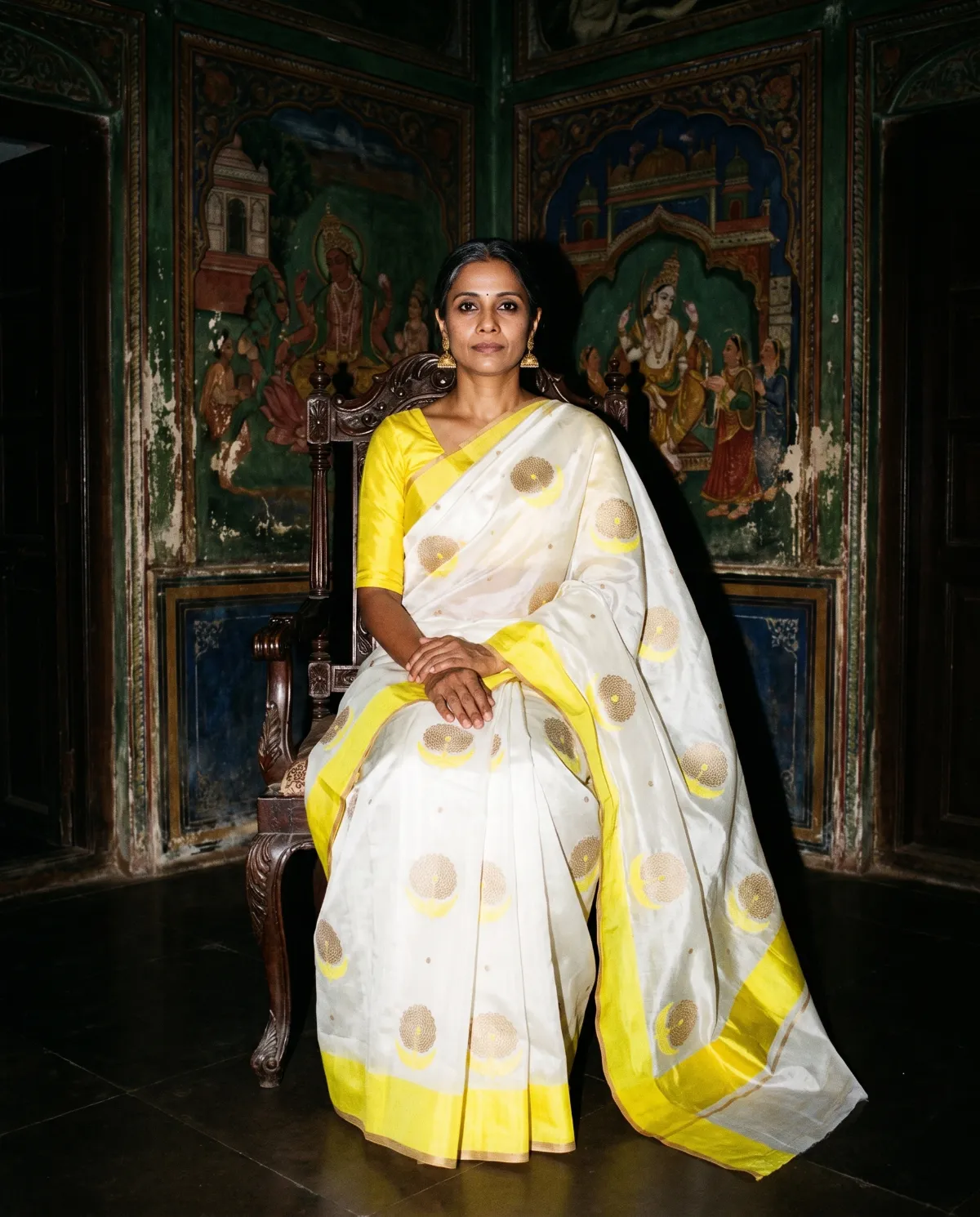 A woman in an ivory sari seated in a painted room at night